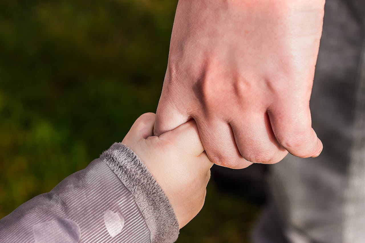 About A close-up of a child and parent holding hands in a park, symbolizing love and trust.