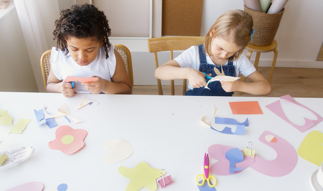 Home Two children crafting colorful paper shapes, focusing on creativity and fun in an indoor setting.