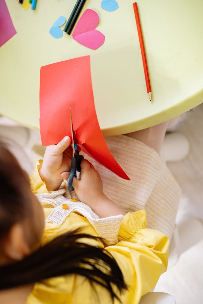 Home Top view of a girl cutting colored paper during a creative arts and crafts session indoors.